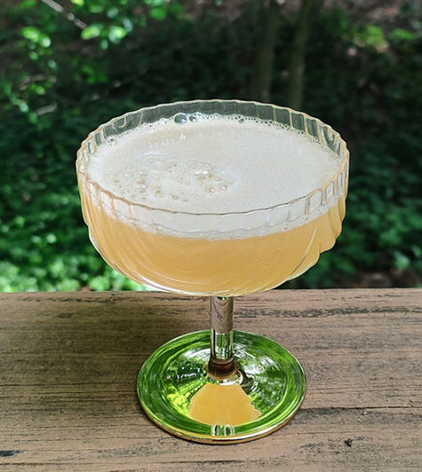 A kitchen bar shows a white quartz countertop, mixed blue collage tile backsplash, and a large collection of spirits, bar accessories, and shot glasses.