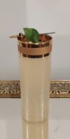 Mojito in a tall vintage glass with wide gold bands around the rim, set on a Hollywood-style vintage tray and garnished with lime and mint held by a vintage Toledo sword cocktail pick.